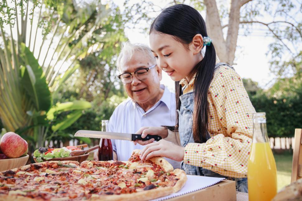 Free Image of Granddaughter enjoying slicing pizza for retirement grandfather 