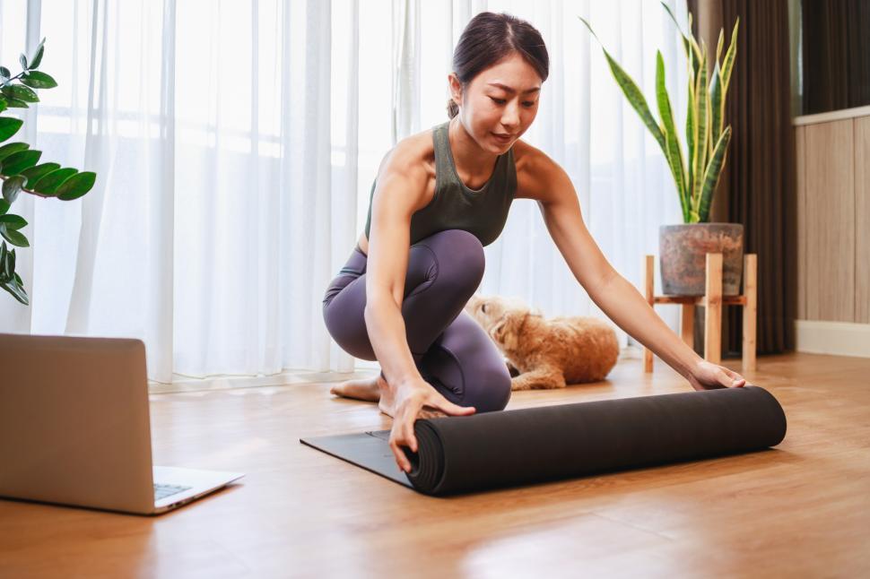 Download Free Stock Photo of Young woman unrolling roll black yoga mat for online training 