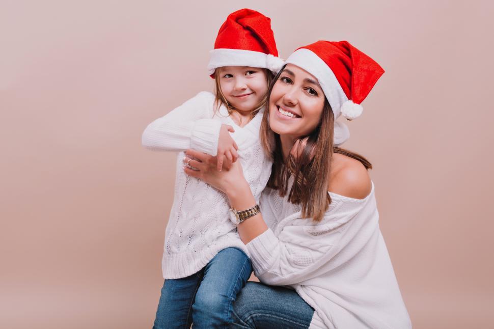 Free Image of Pretty mother with cute daughter wearing white pullovers and Santa Claus caps 