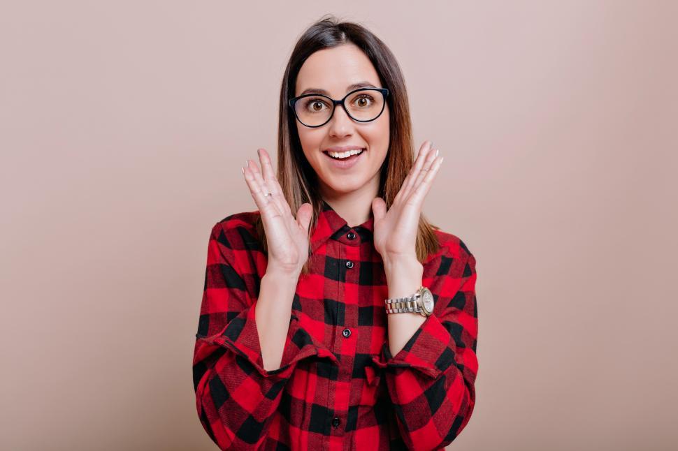 Free Image of Young woman in checkered shirt and glasses with surprised emotions and raised up hands 