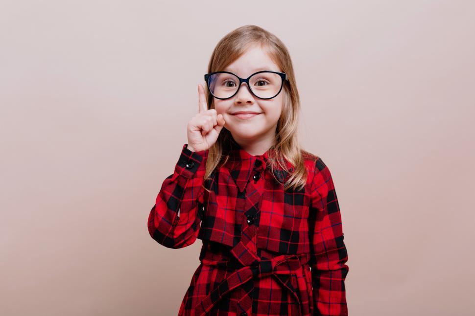 Free Image of Girl wearing glasses and checkered shirt raised up one finger and smiles at the camera 