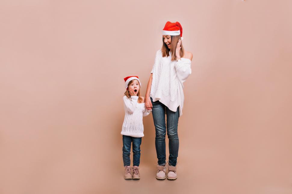 Free Image of Girl and mom in Santa caps holding each other on hands 