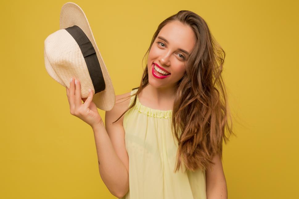 Free Image of Long-haired female model posing on yellow background, holding straw hat 
