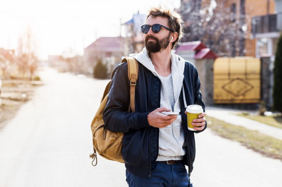 Free Image of Man with beard and sunglasses typing message and walking in the countryside 