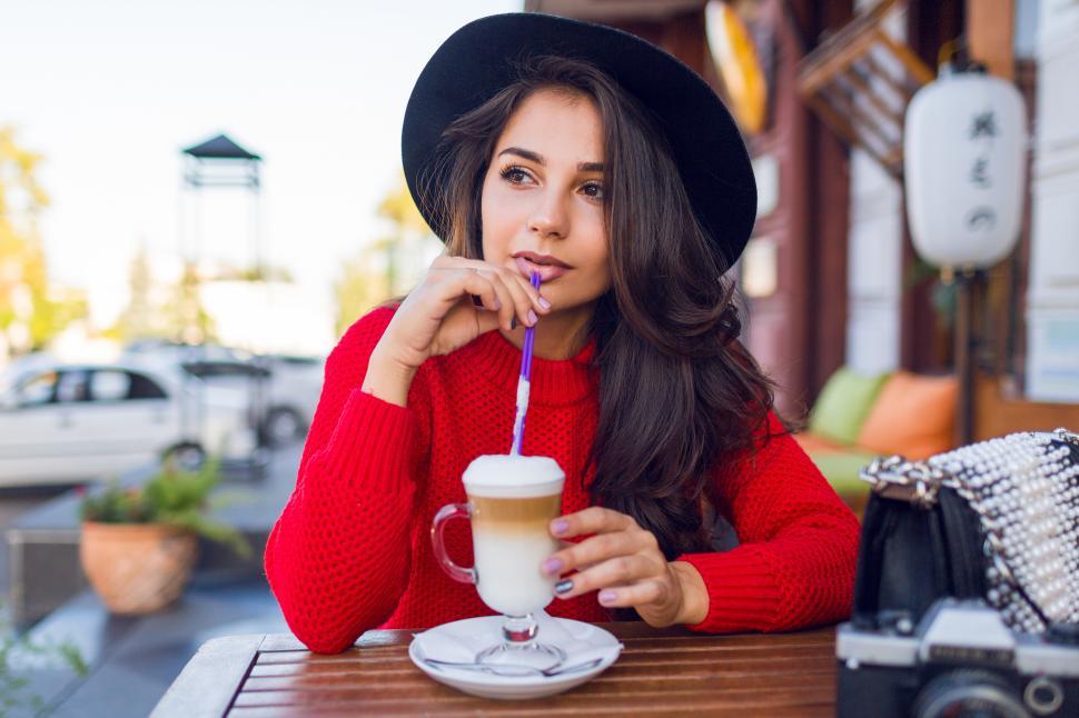Free Image of Young lady in stylish black hat and bright red sweater sitting in open space cafe drinking coffee 