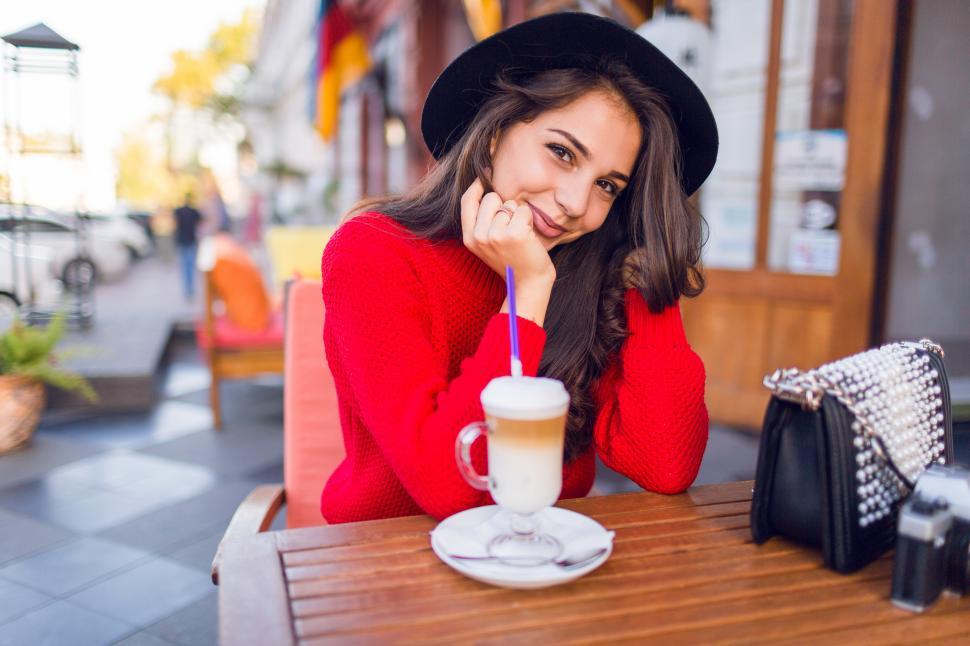 Free Image of Close up beautiful young brunette woman in stylish black hat at streetside cafe table 