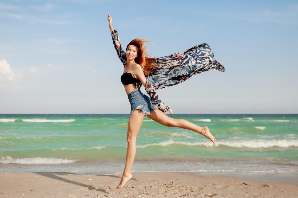 Free Image of Carefree woman jumping on white sandy beach 