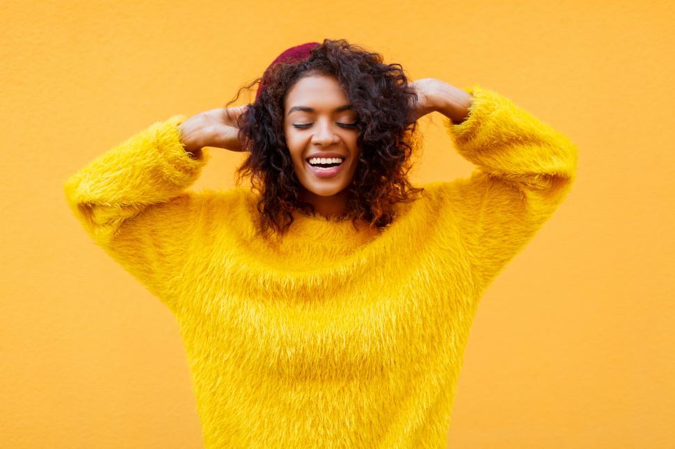 Free Image of Smiling woman with closed eyes playing with her curly hair on yellow background 