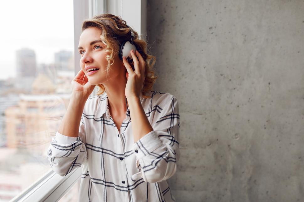 Free Image of Woman listening music by earphones, posing near window 