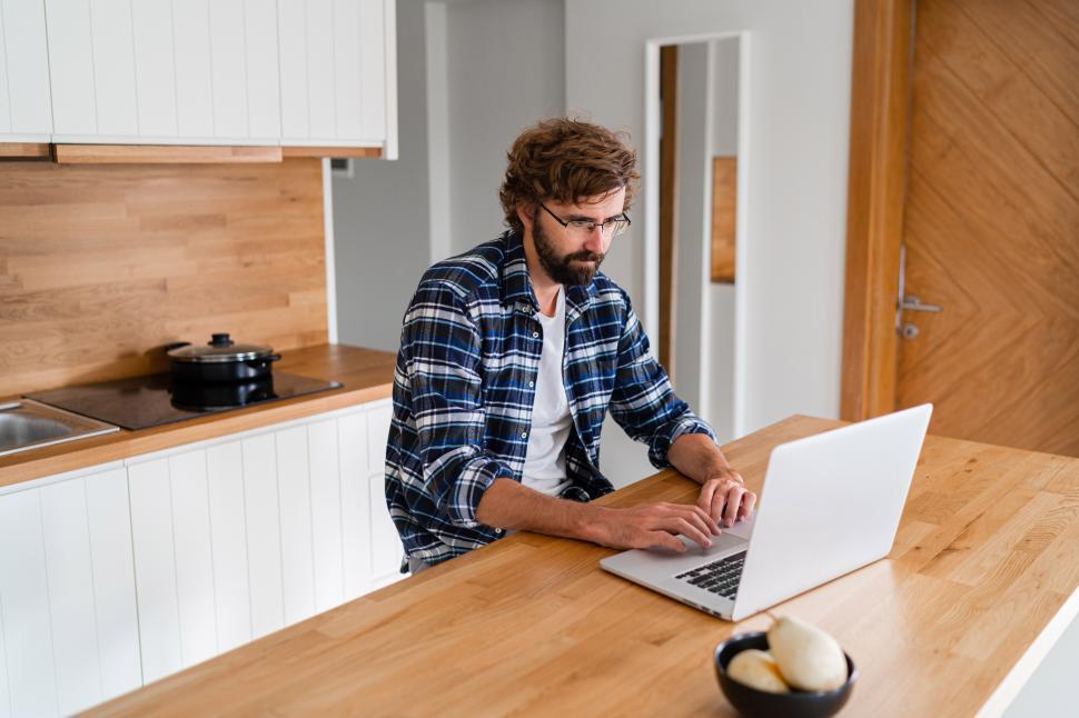 Free Image of Man with beard in plaid shirt using laptop in the kitchen 