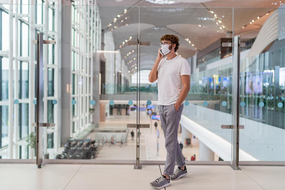 Free Image of Man wearing face mask in airport and talking by smartphone 