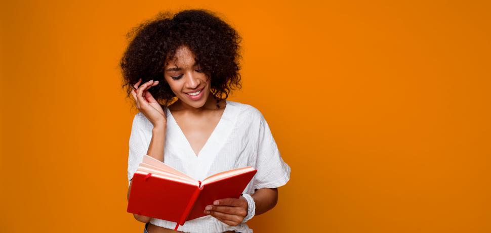 Free Image of Female student reading book against orange wall 