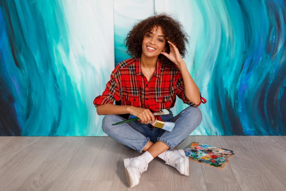 Free Image of Student  holding brushes and posing over her abstract artworks on canvas 
