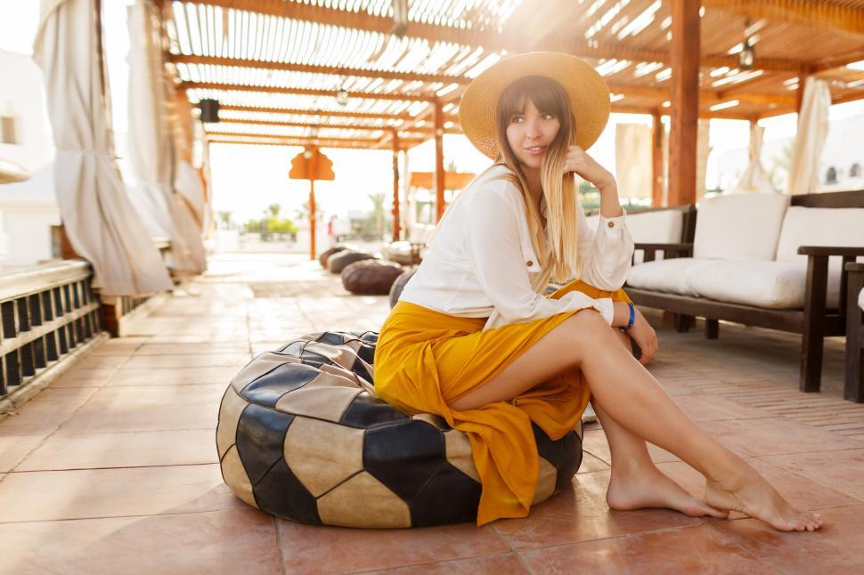 Free Image of Bohemian woman in straw hat sitting on pillows in stylish authentic resort in Egypt 