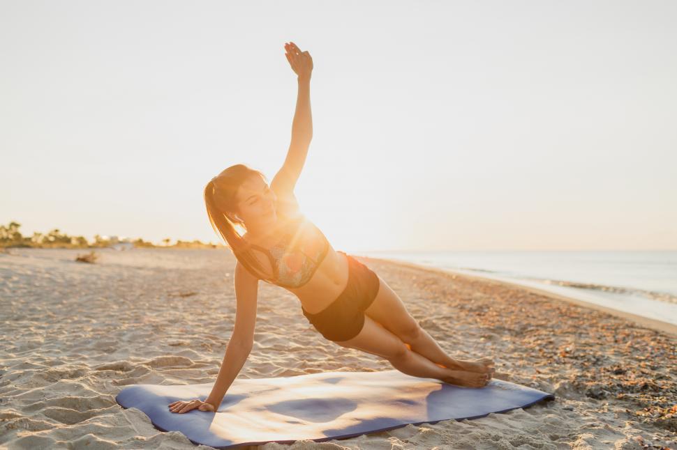 Free Image of Fit woman doing yoga on the beach at sunset 