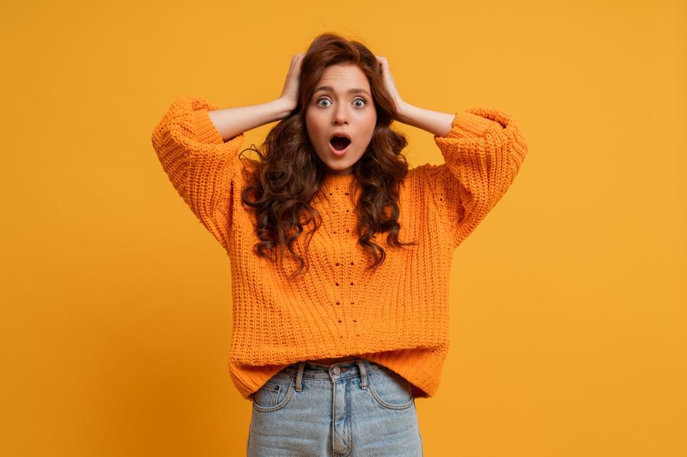 Free Image of Young girl in orange sweater  posing in studio looking exasperated 