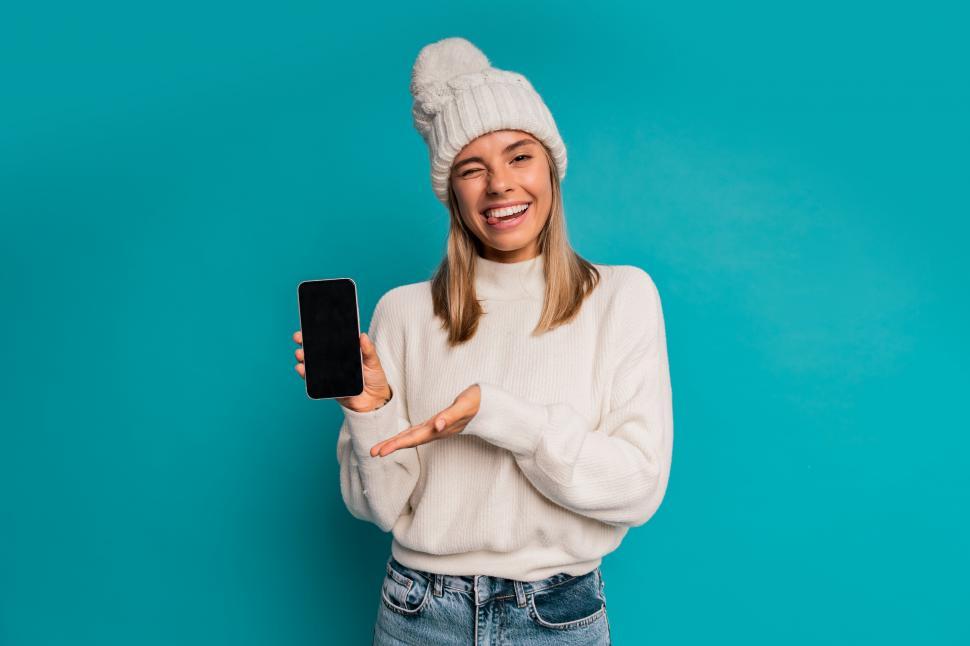 Free Image of Portrait of smiling blond woman in white hat and wool sweater  a holding mobile phone 