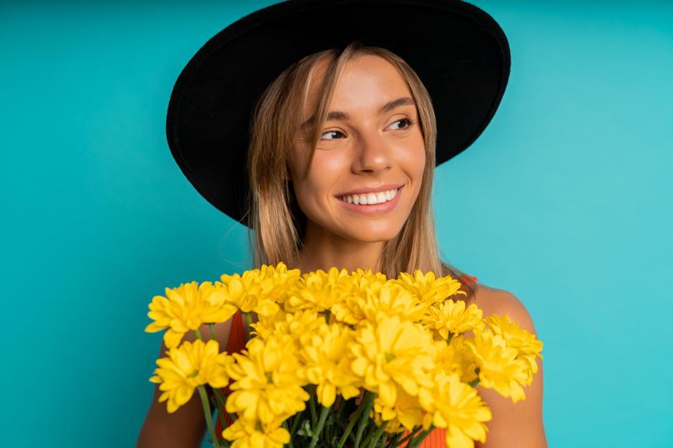 Free Image of Woman posing with yellow flowers over blue background in studio 
