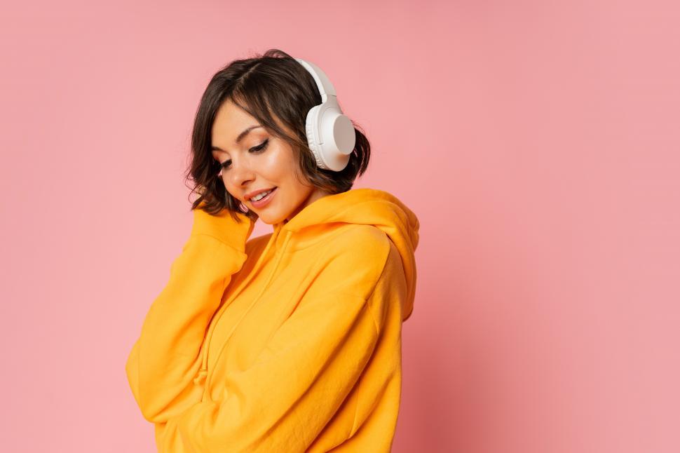 Free Image of Woman in white earphones listening to music on pink background 