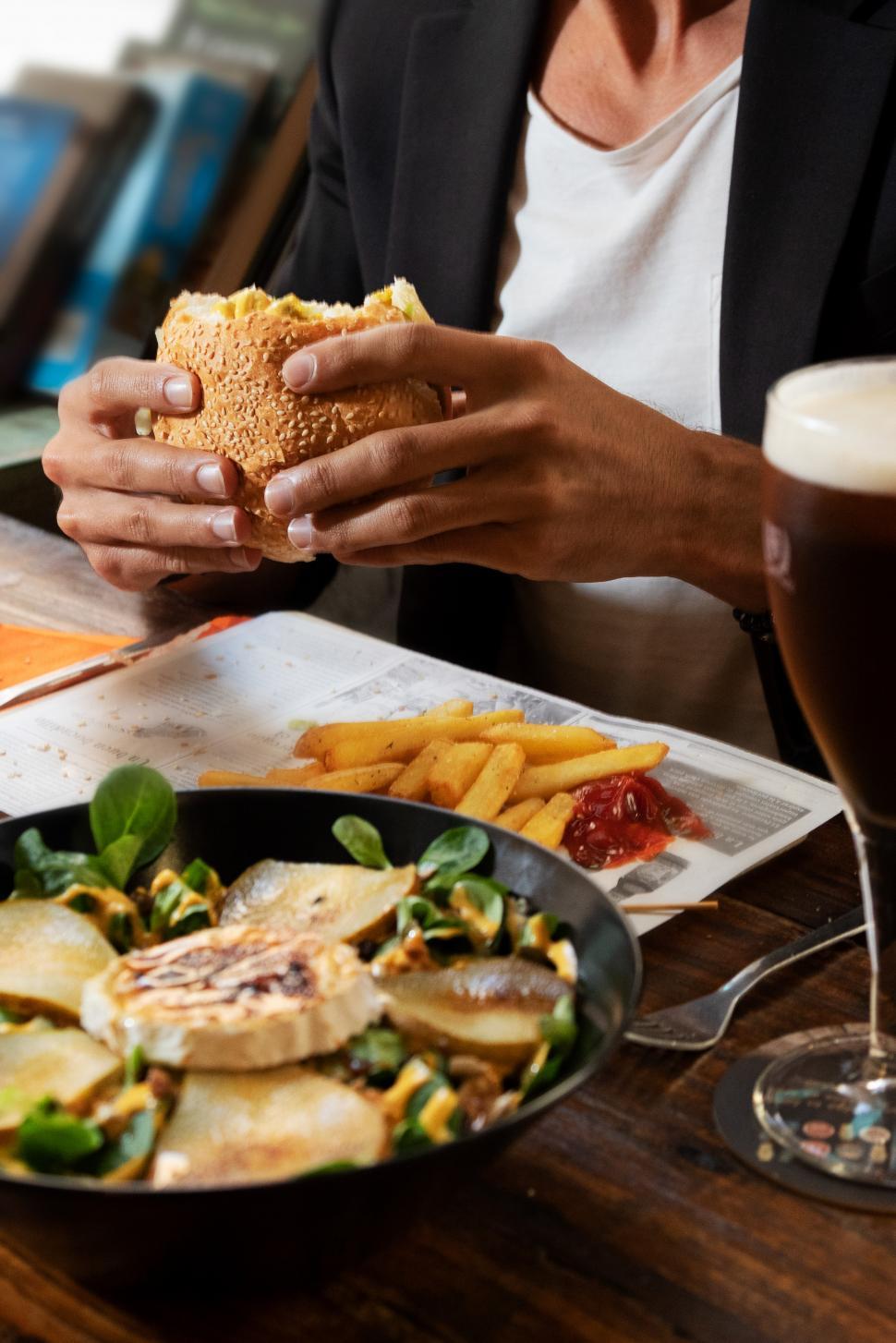 Free Image of a man eating in a pub, holding a burger 