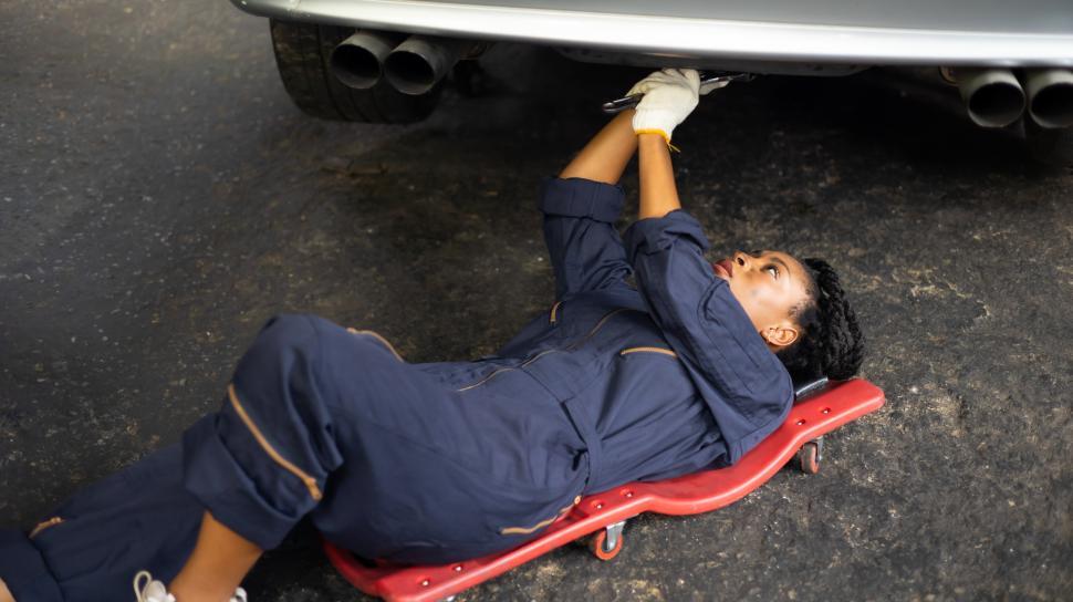 Free Image of Young female mechanic on a creeper under a car 