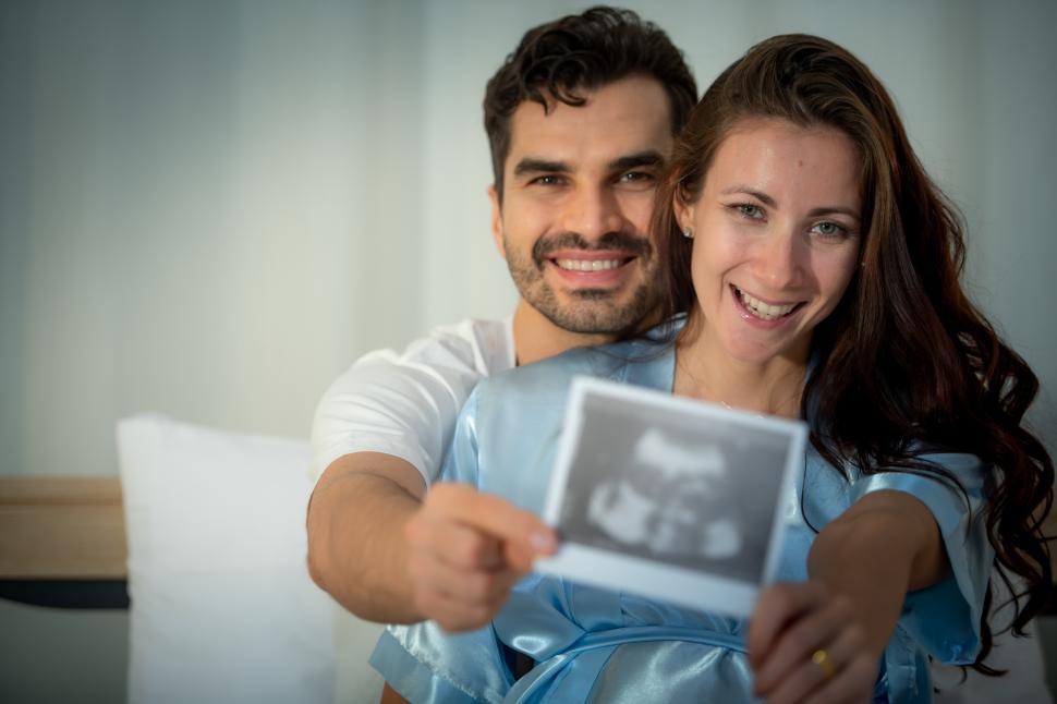 Free Image of Pregnant couple showing off sonogram of their unborn child 