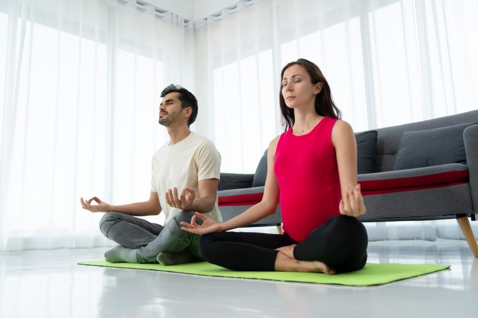 Free Image of A pregnant woman and her partner meditate in a living room. 