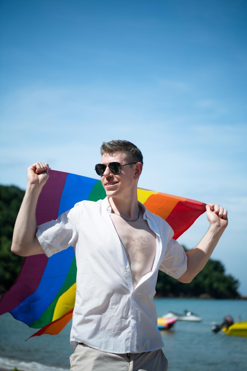Free Image of Young man holding rainbow flag - Pride at the beach 