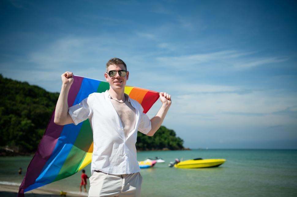 Free Image of Young man at the beach, holding rainbow pride flag 