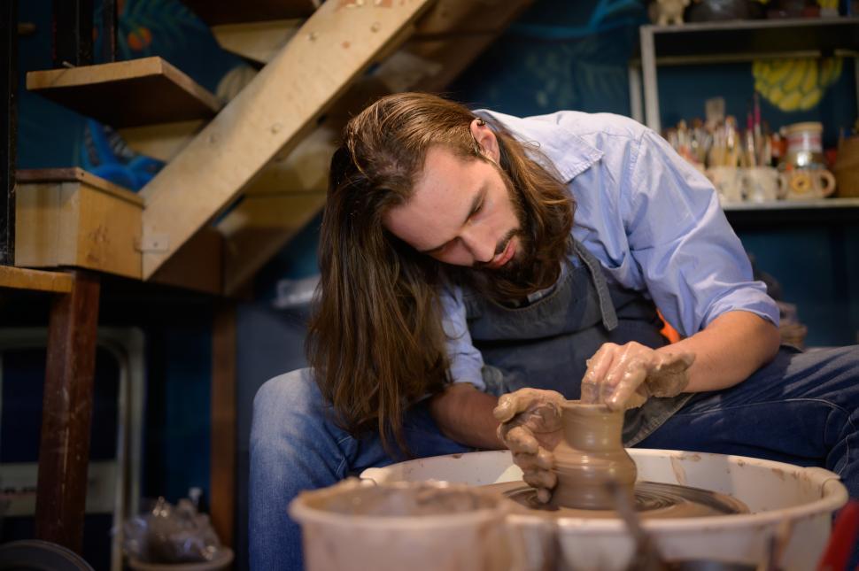 Free Image of Potter hunched over pottery wheel, thorwing pots from wet clay 