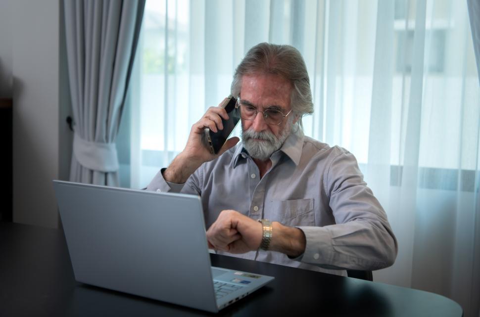 Free Image of Middle aged man working at home, checking time while on the phone 