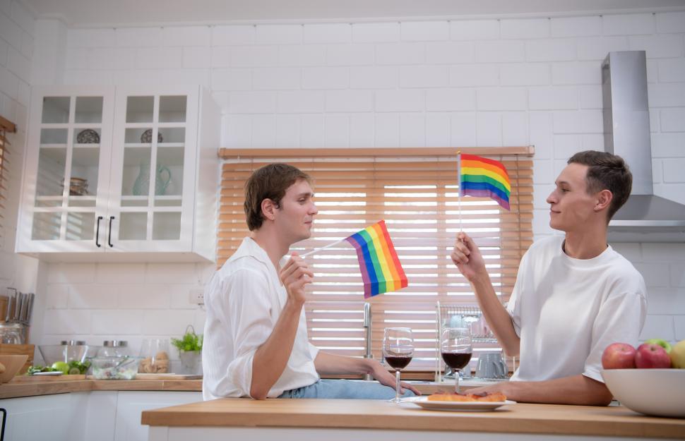 Free Image of Young couple hanging out in the kitchen, waving small pride flags 