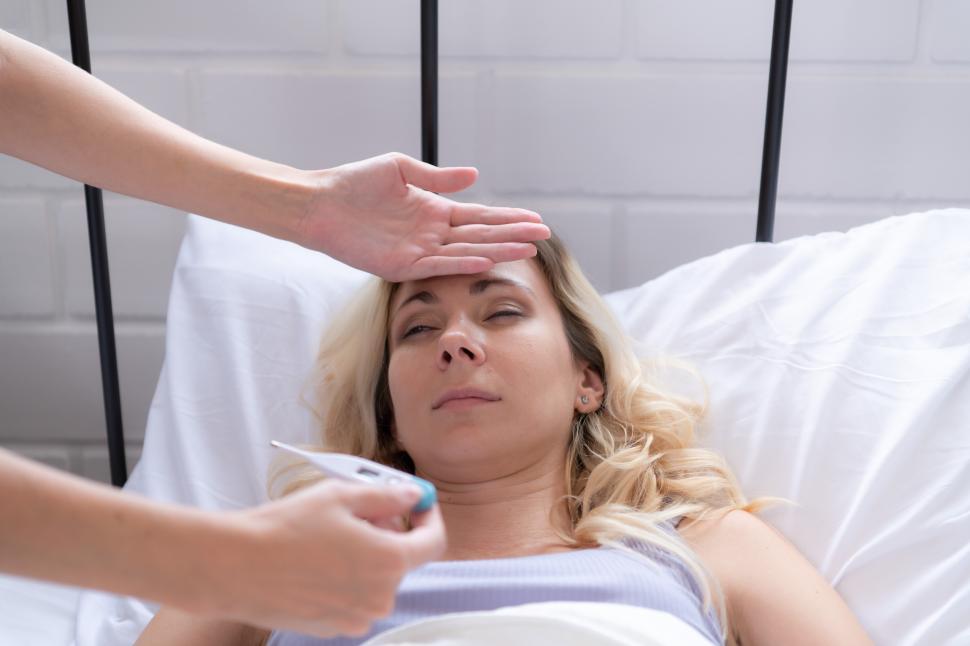 Free Image of Woman sick in bed, tended to by her partner, taking her temperature 