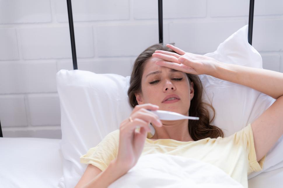 Free Image of Woman is sick and taking her temperature while in bed  