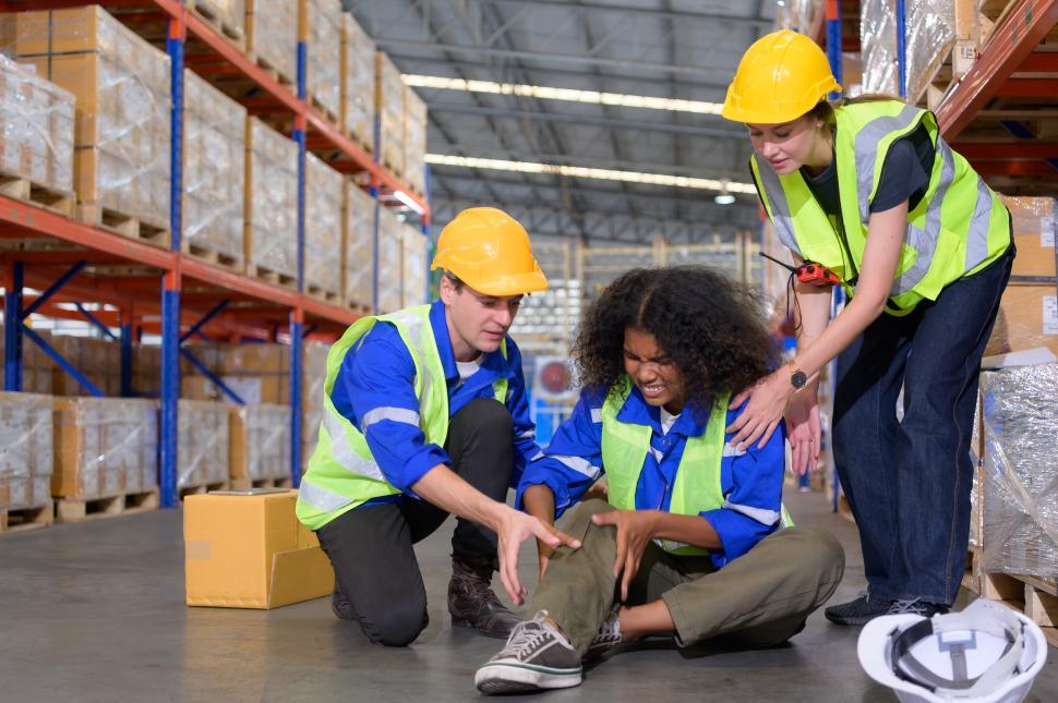 Free Image of Injured worker in large warehouse, surrounded by coworkers 