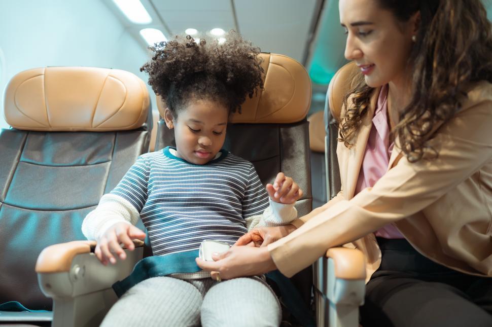 Free Image of A mother assists her youngster in fastening the airplane seatbelt 