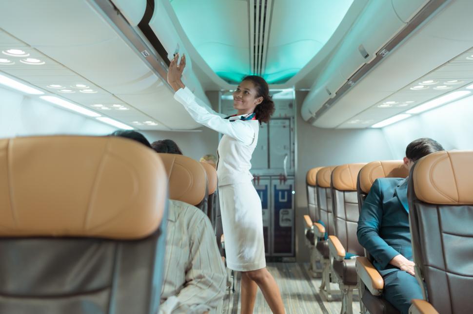 Free Image of Flight attendant checks the passenger overhead luggage before takeoff 