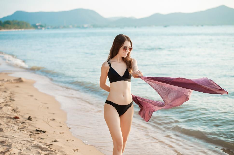 Free Image of Woman in black bikini is walking on the beach, enjoying cool summer breeze 