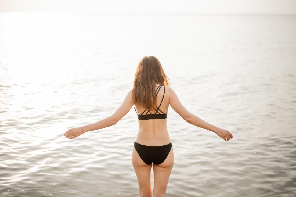 Free Image of Woman in black bikini is walking into the surf on a clear day 
