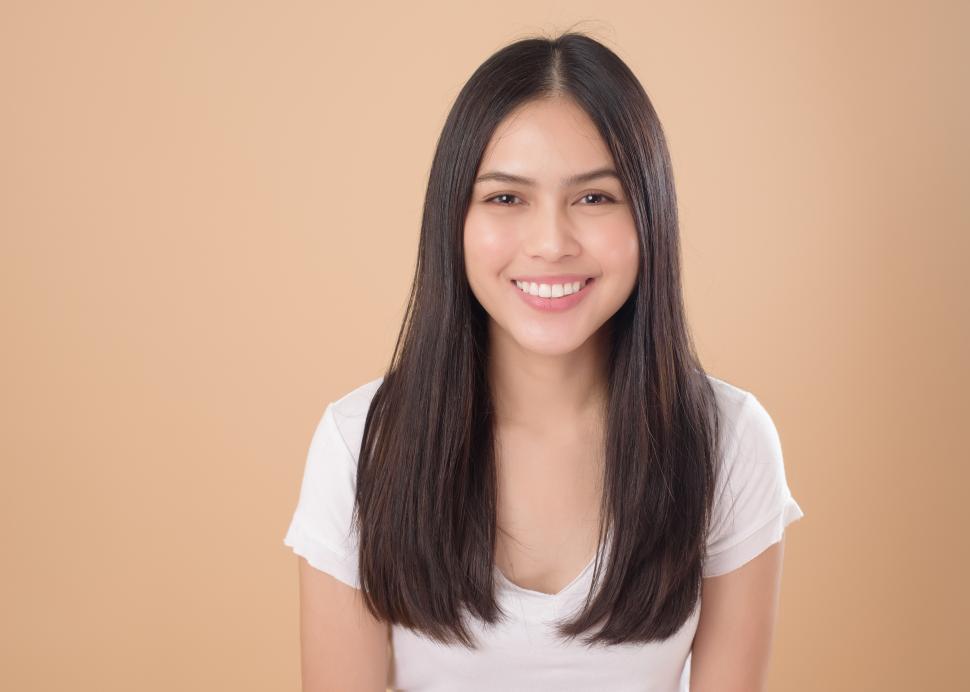 Free Image of A Portrait of smiling Asian woman with white T-shirt over light brown background 