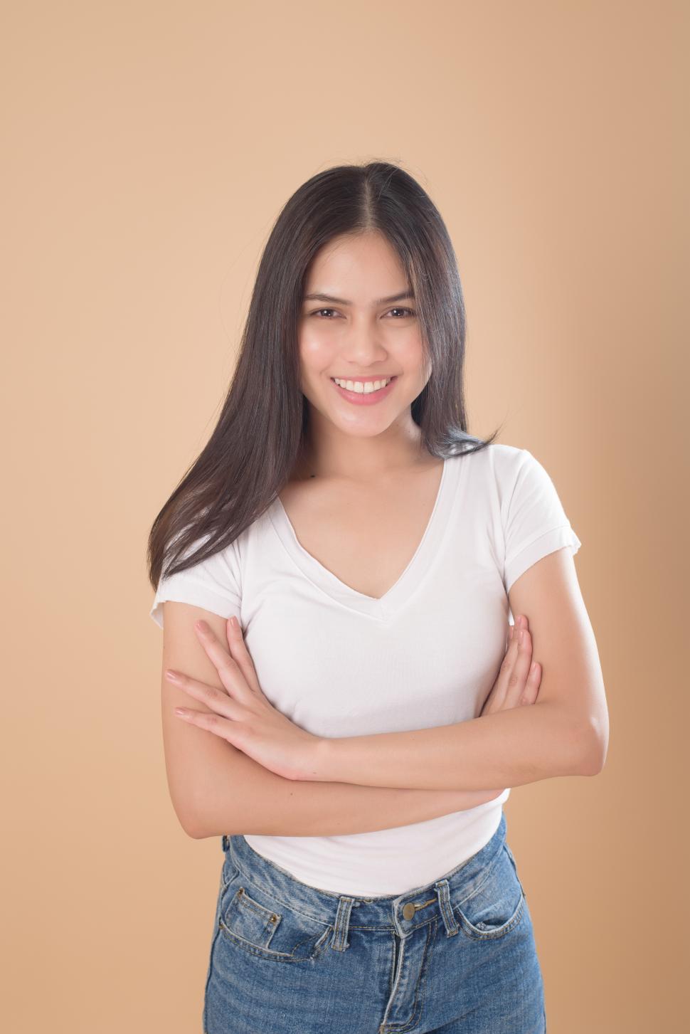Free Image of Smiling young woman with arms crossed over light brown background 