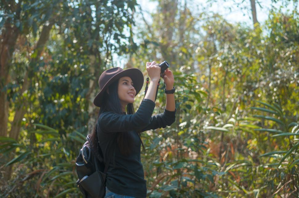 Free Image of Young woman trekker taking photos of nature with camera in the woods 