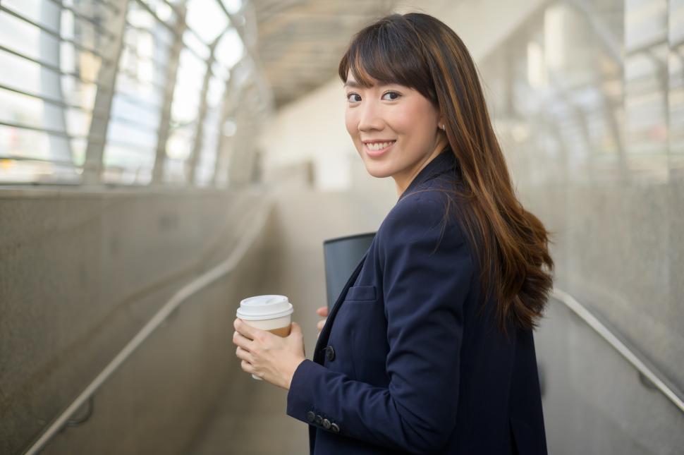 Free Image of Successful businesswoman carrying coffee looks back over her shoulder 