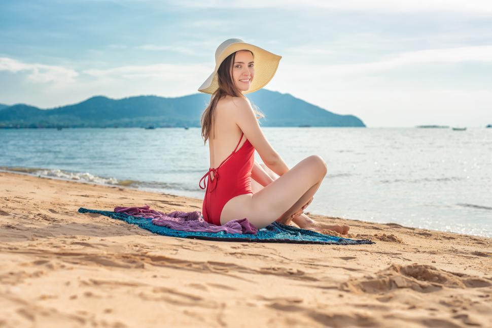 Free Image of Woman in red swimsuit is sitting on a towel or blanket on the beach 