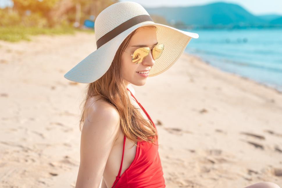 Free Image of Woman in sun hat and sunglasses walking on the beach during summer vacation 