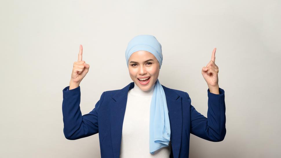 Free Image of close up of young muslim businesswoman with hijab pointing up at copyspace 