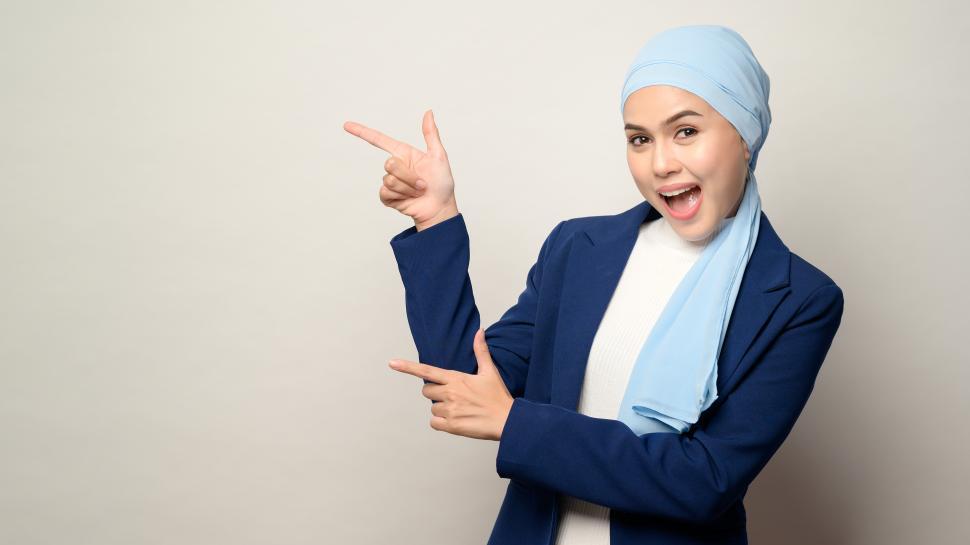 Free Image of Muslim businesswoman with hijab pointing with both hands at blank copyspace 