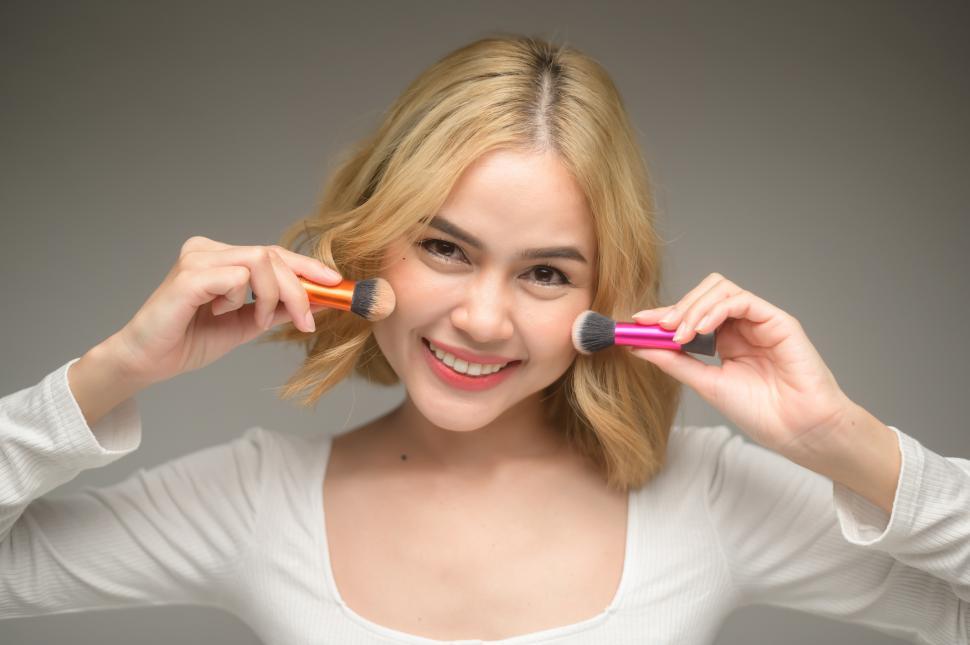 Free Image of Young blonde woman holding cosmetic brushes up for camera 