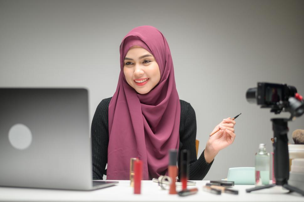 Free Image of Muslim woman entrepreneur working with laptop presents cosmetics to viewers 