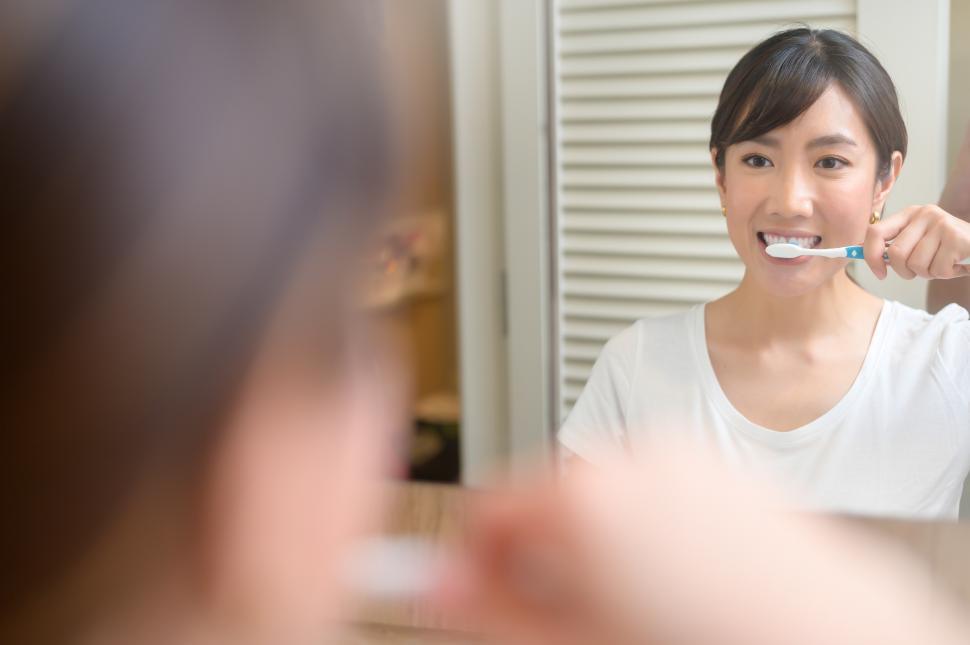 Free Image of Portrait of young woman brushing her teeth in the mirror in the bathroom 